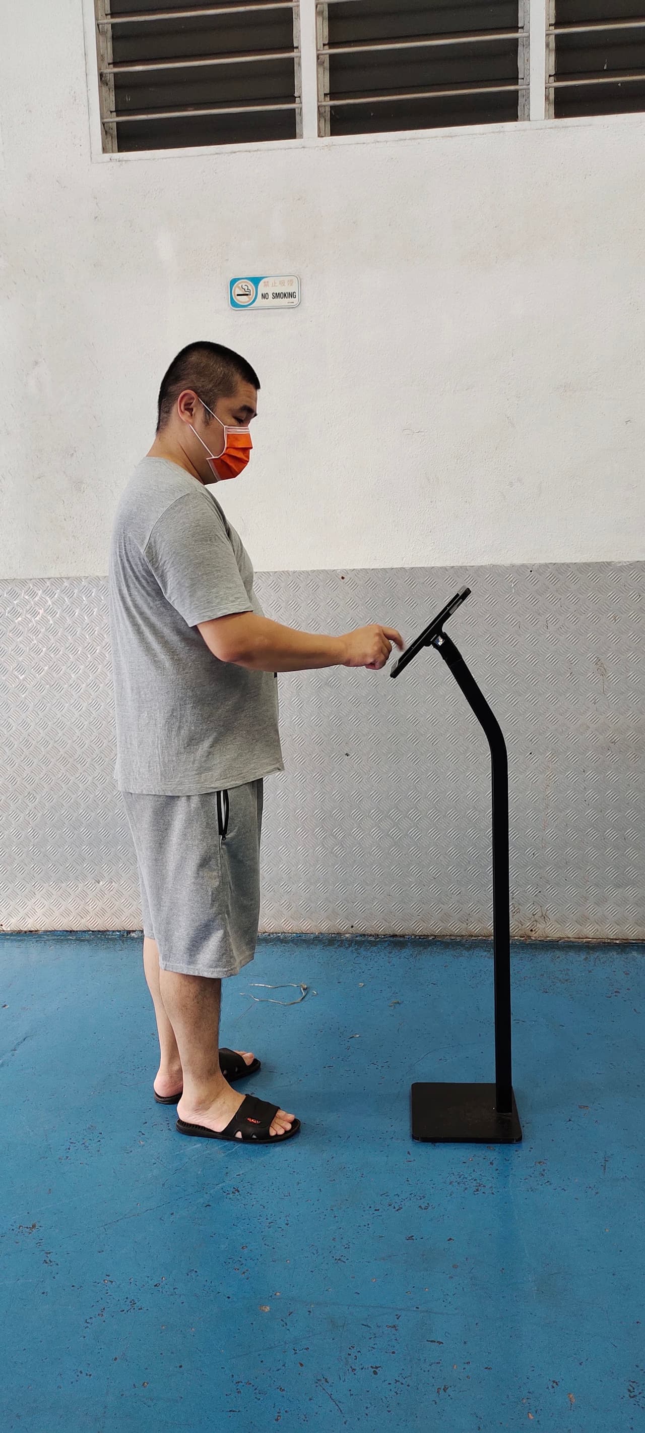 A person standing beside an iPad floor stand, showing its height relative to an adult