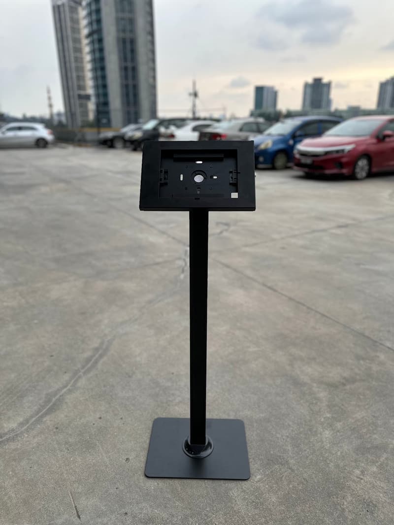 iPad floor stand standing on tarmac outdoors with parked cars behind