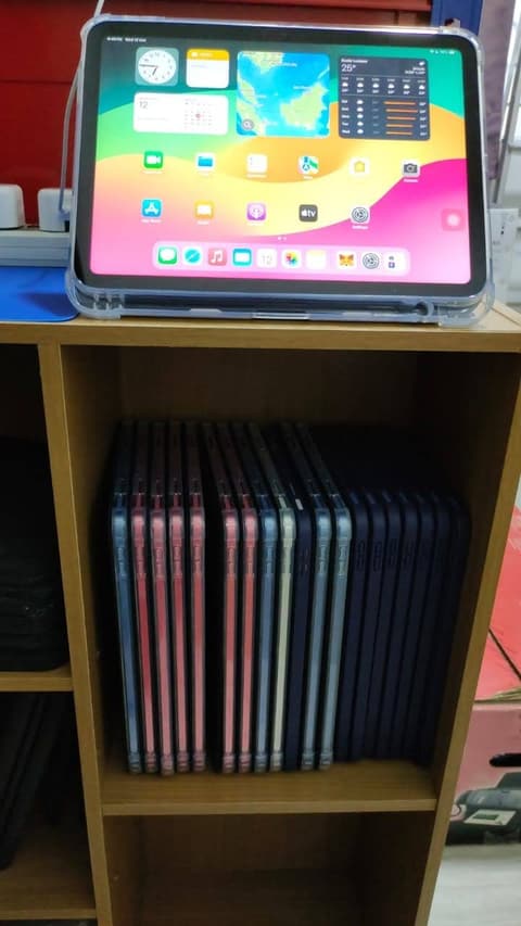 An iPad standing on a shelf above a row of stacked iPads in storage