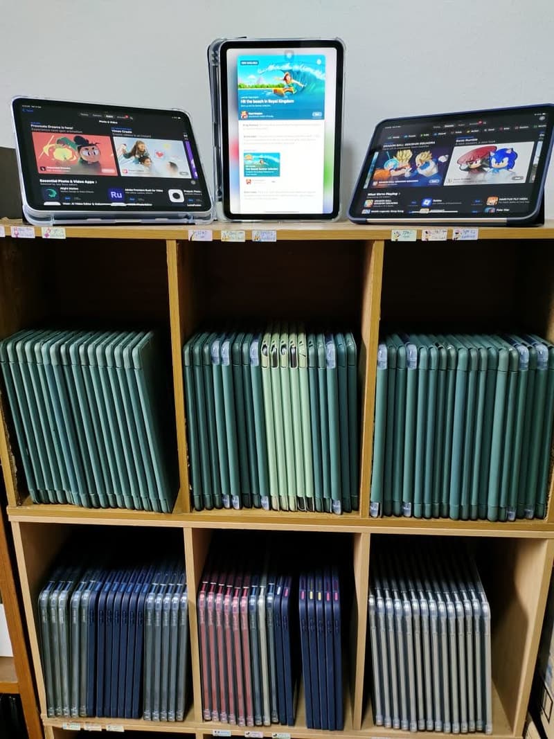 Shelving full of cased iPads with several units switched on and standing on top