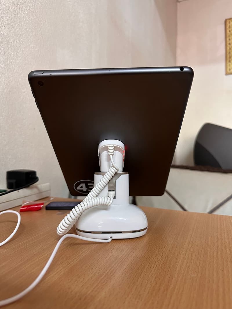 Back view of a white alarmed iPad stand showing the sensor head, indicator light and coiled cable