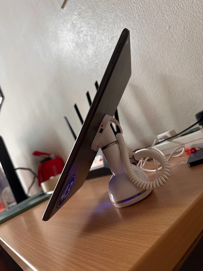 Side view of a white alarmed iPad stand showing its tilt angle on a desk